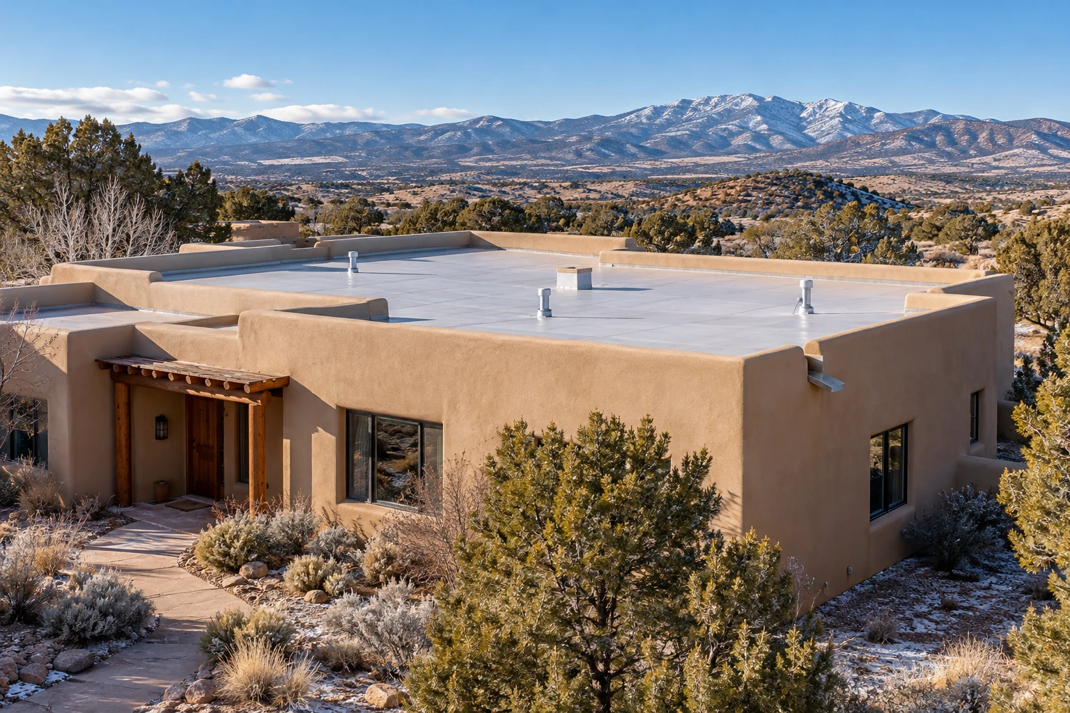 New Mexico stucco home with a low-slope roof and clear parapet drainage outlet before winter weather.